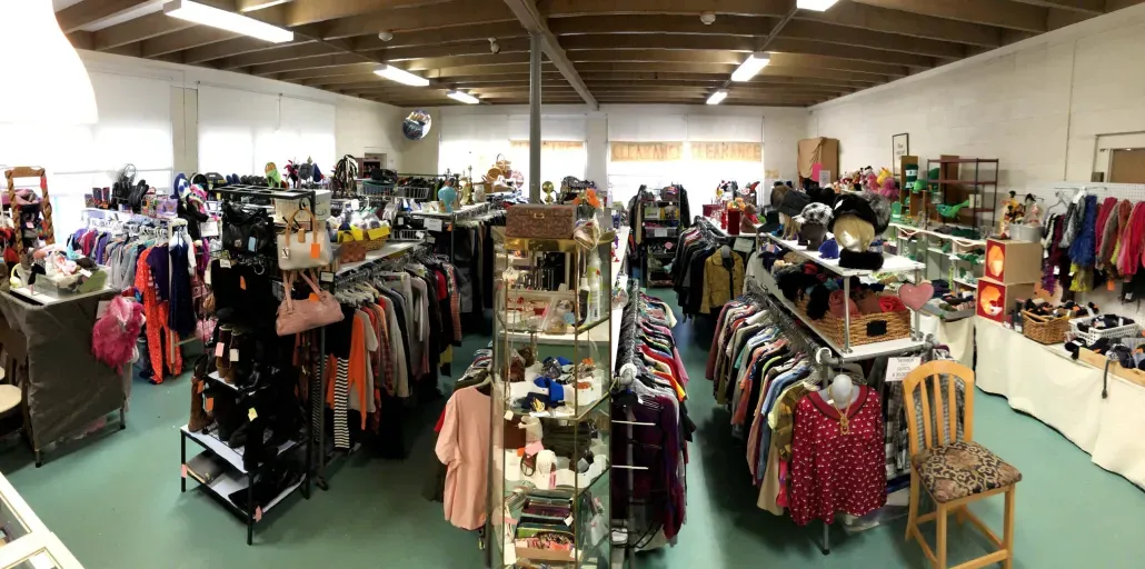 Thrift shop with rows of shirts on hangers and shoes in rows.
