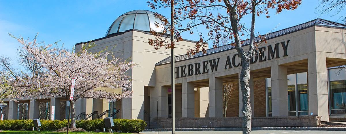 A Hebrew Academy building with a domed roof, stone columns, landscaped grounds and blooming trees.