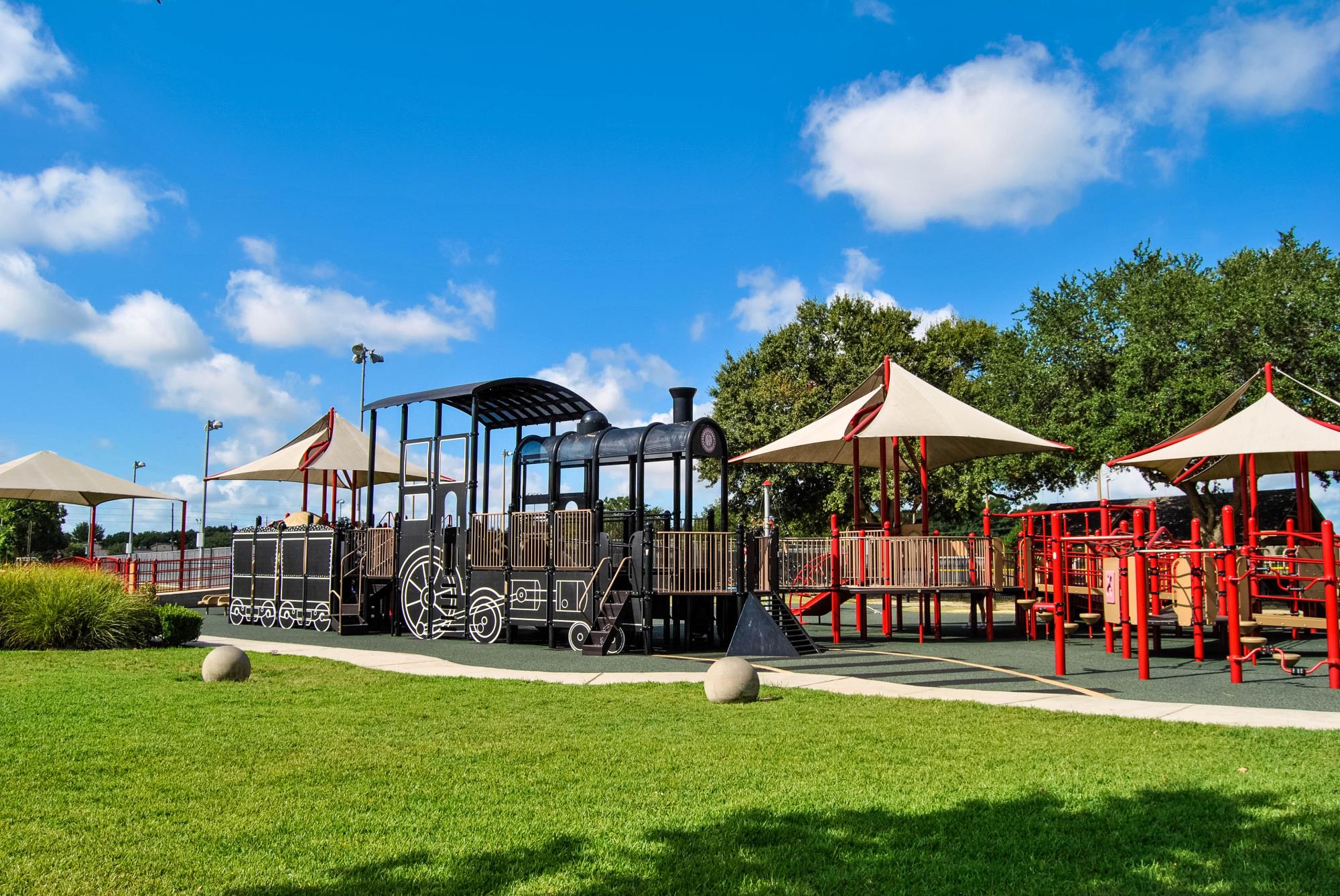 A large outdoor playground with covered play structures, a train-themed climbing area and grassy surroundings.