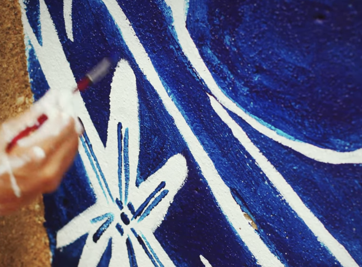 Blue and white mural being painted on cement wall.