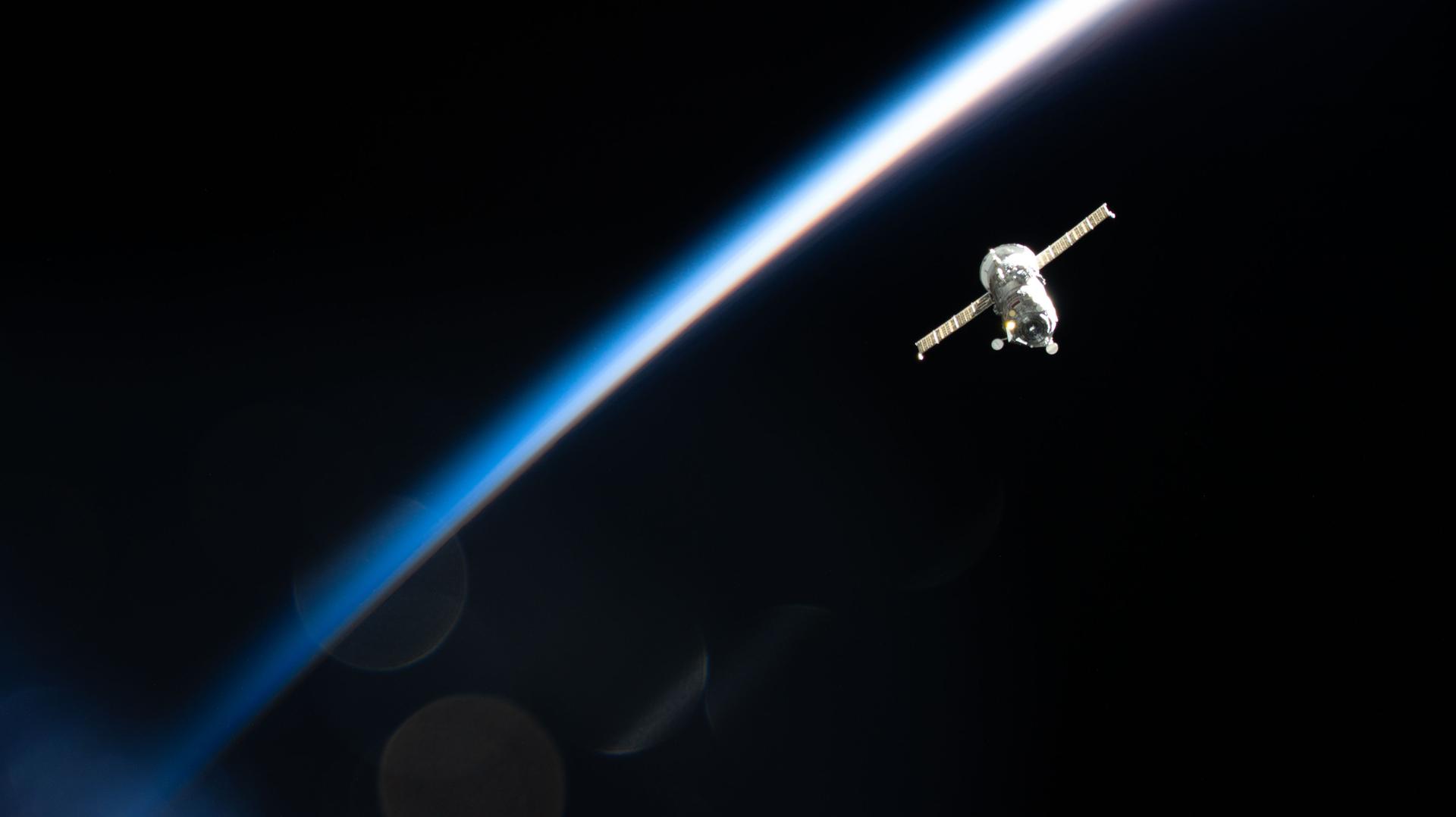 Spacecraft orbiting above Earth’s curved horizon, with the planet’s blue atmosphere glowing against the darkness of space.