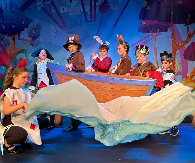 Kids performing on a stage waving a sheet and sitting in fake boat.