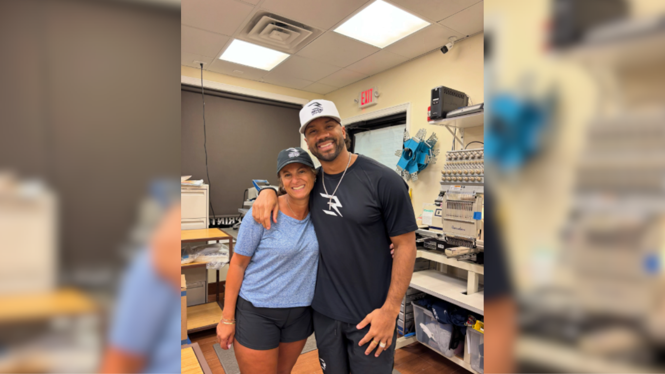 Retired NFL quarterback Russell Wilson poses with a woman inside a custom apparel business.