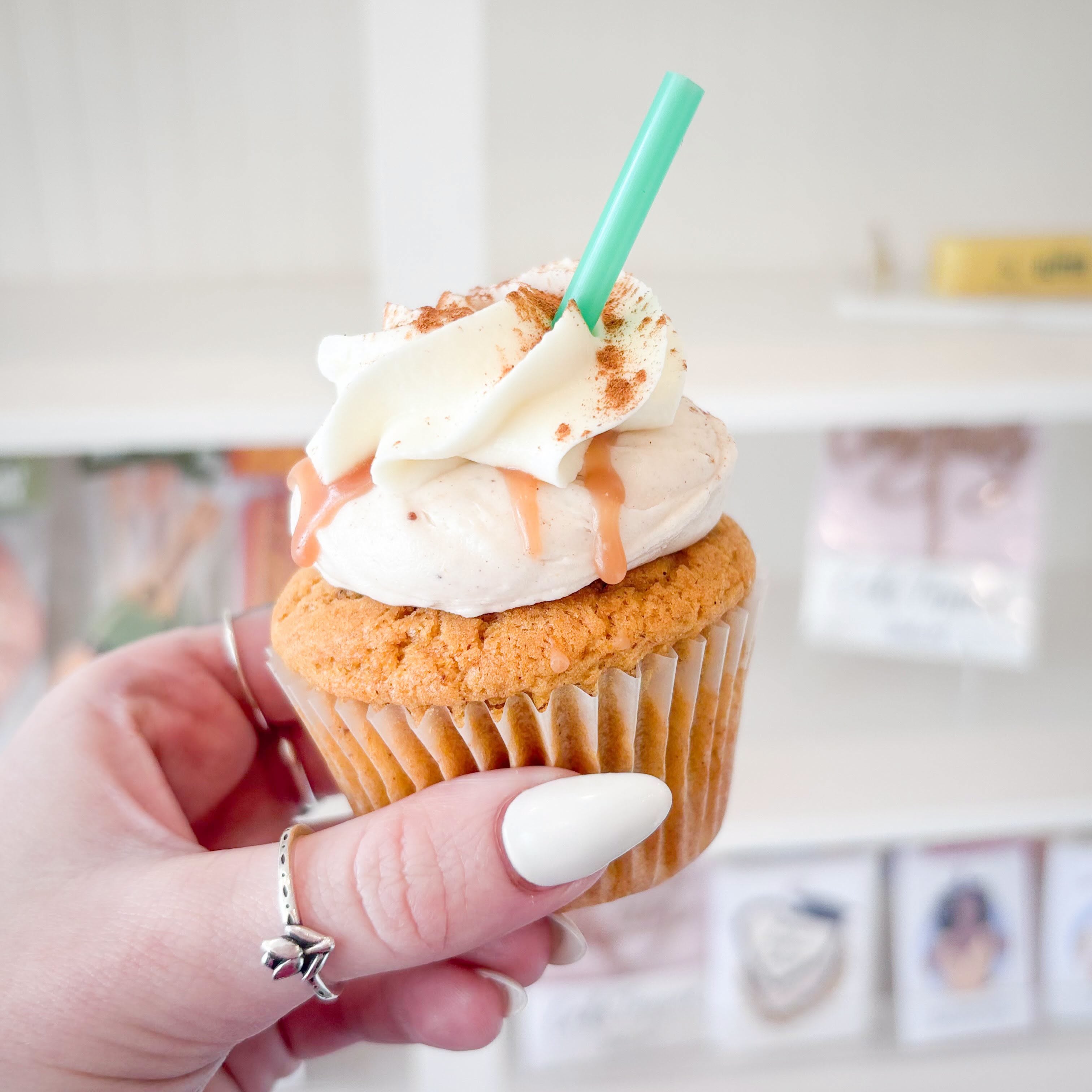 Cupcake with white frosting held by woman with ring on and white nail polish