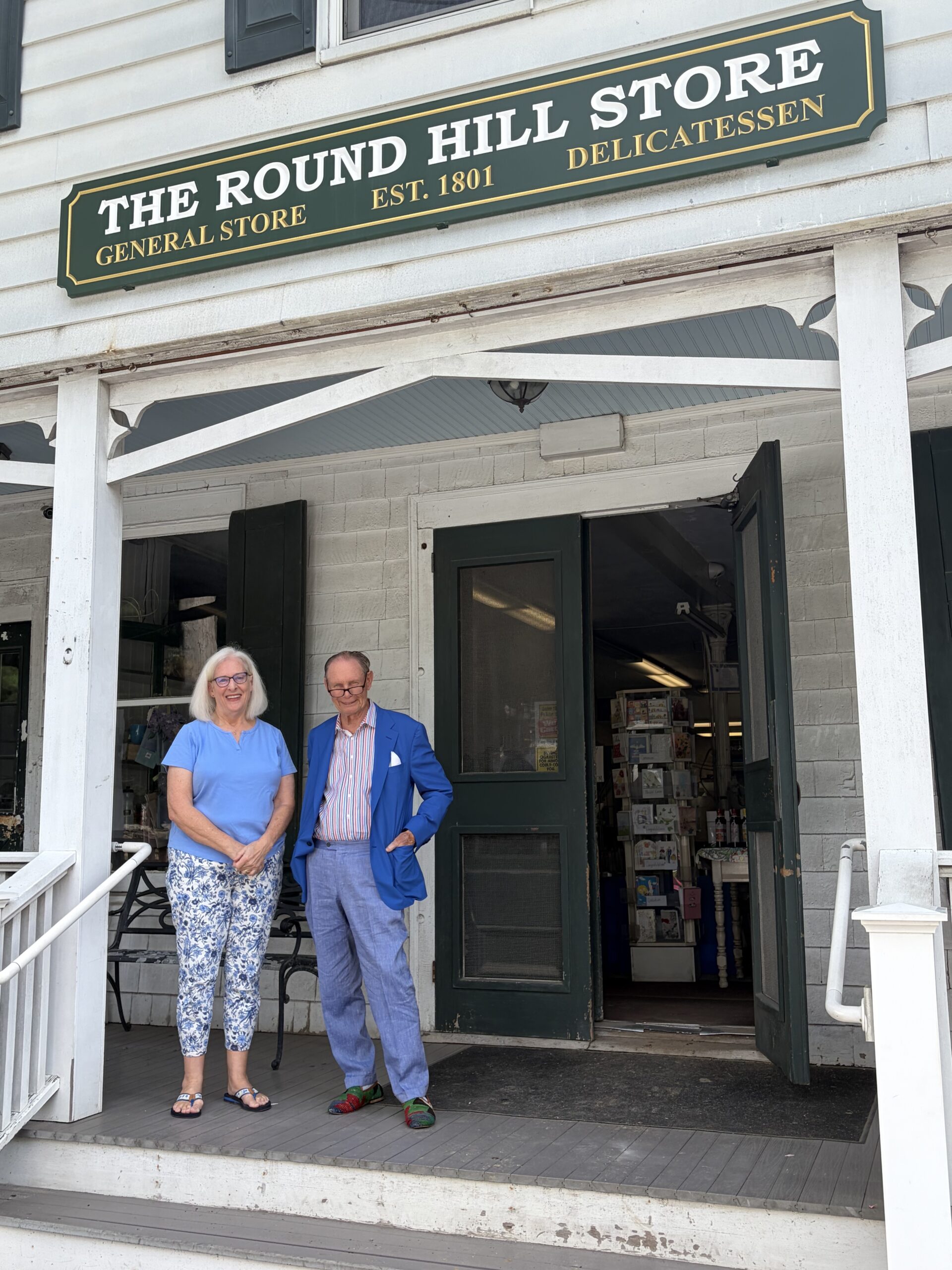 Man and woman stand outside white storefront with green sign.
