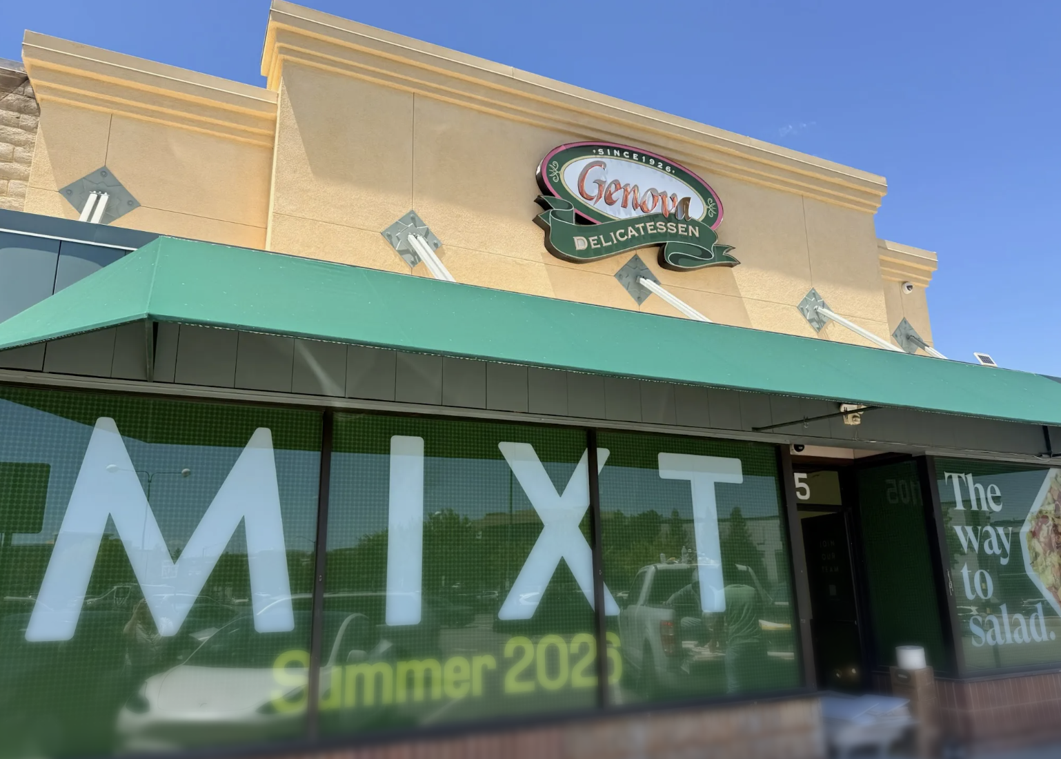 Storefront of Genova Delicatessen, a since-1926 deli, with a green awning below and windows advertising "MIXT Summer 2026"