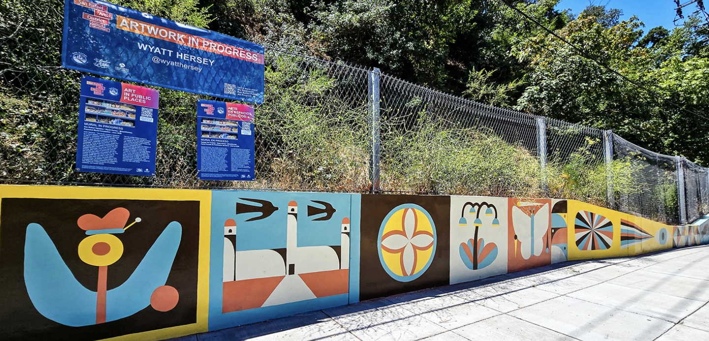 "San Rafael Tapestry" mural by Wyatt Hersey along the Second Street retaining wall, showing colorful stylized panels of local wildlife, flowers, and geometric patterns in blue, yellow, orange, and brown.