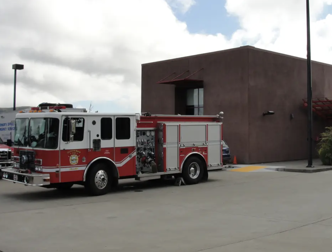 A red and white Southern Marin Fire District fire engine parked outside a fire station building under a partly cloudy sky.