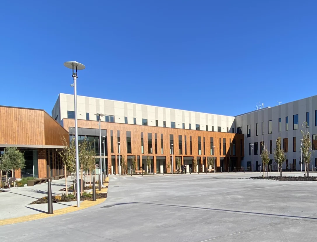 Exterior of a modern medical center building with wood-paneled and light gray facades, and a landscaped plaza in front.