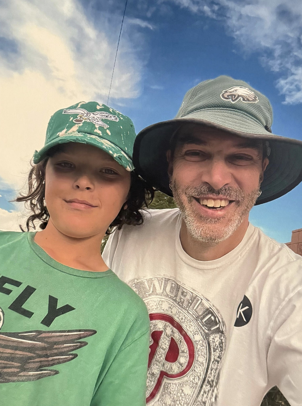 Orion Greene as a young teen with his father, John Greene, both wearing Philadelphia Eagles hats in an outdoor selfie.
