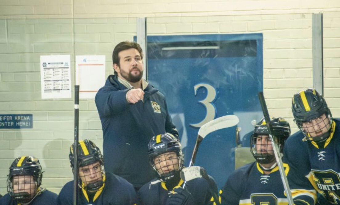 A hockey coach points while directing players from the bench.