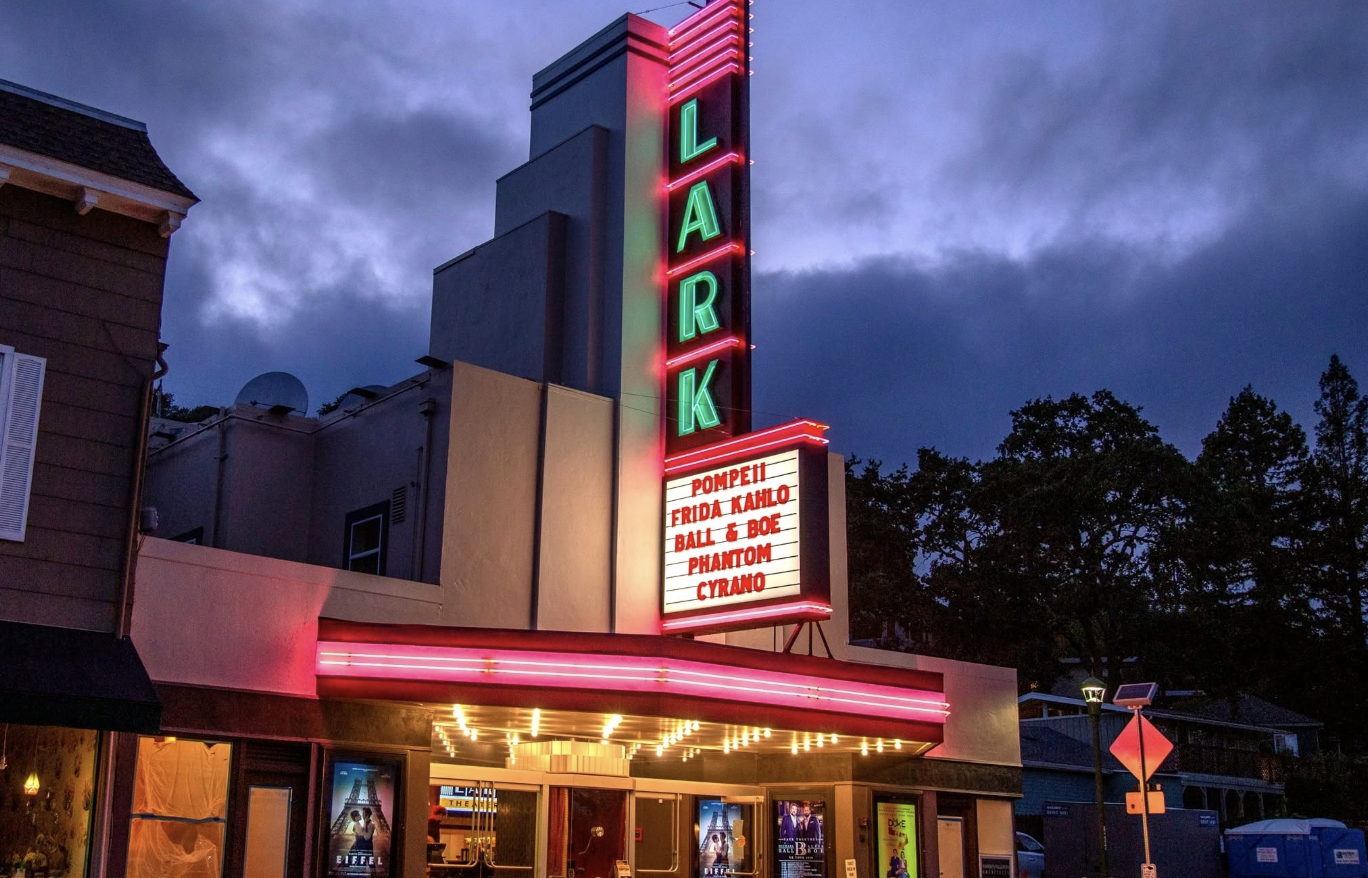 The Lark Theater's illuminated marquee at dusk, with a lit-up "LARK" sign and showtimes listed below.