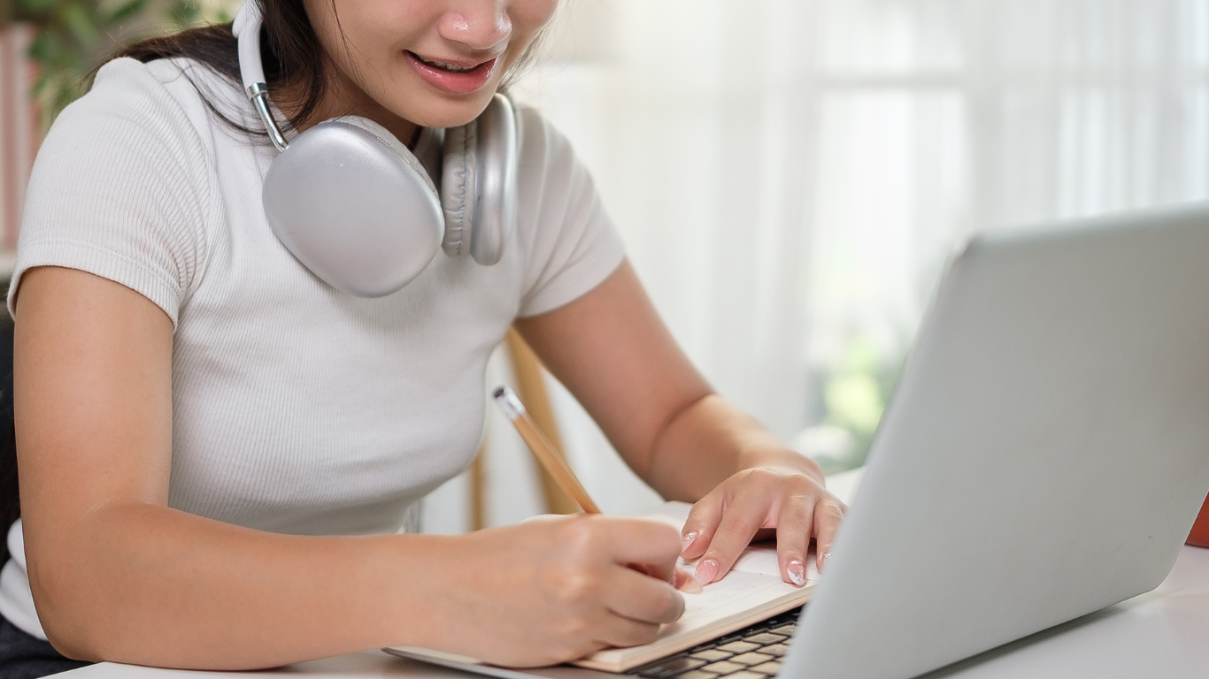 Student on laptop taking notes next to computer