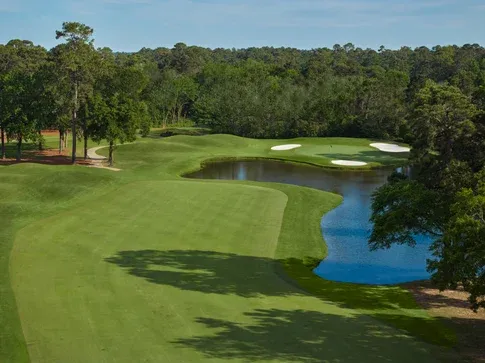A scenic golf course featuring a manicured fairway, water hazard and surrounding trees.