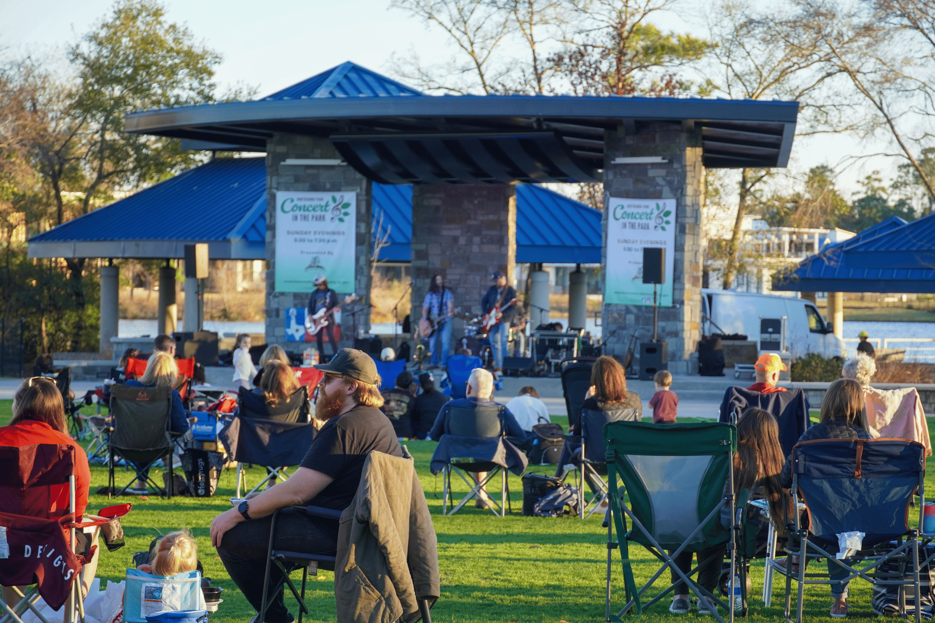 People gather at local park with stage sitting on chairs watching band.