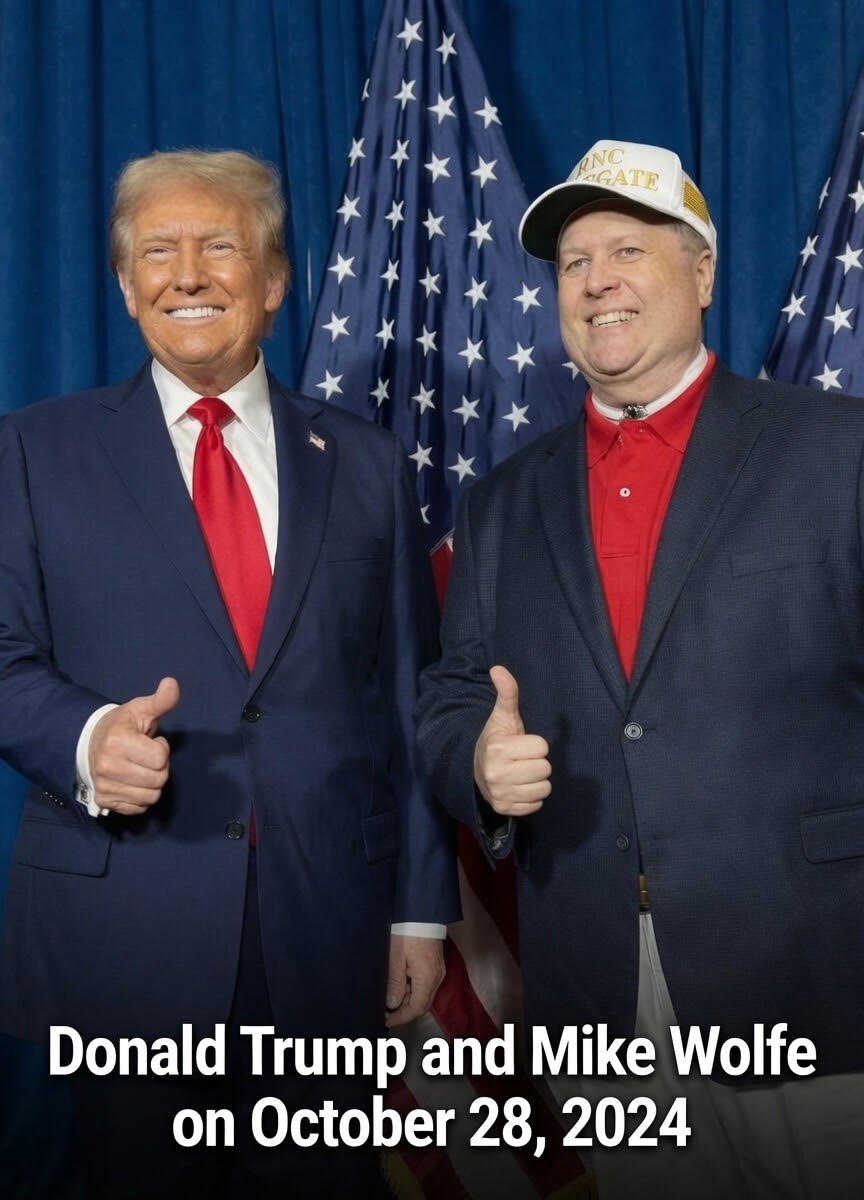 Two men in suits stand in front of American flags, smiling and giving thumbs-up gestures.