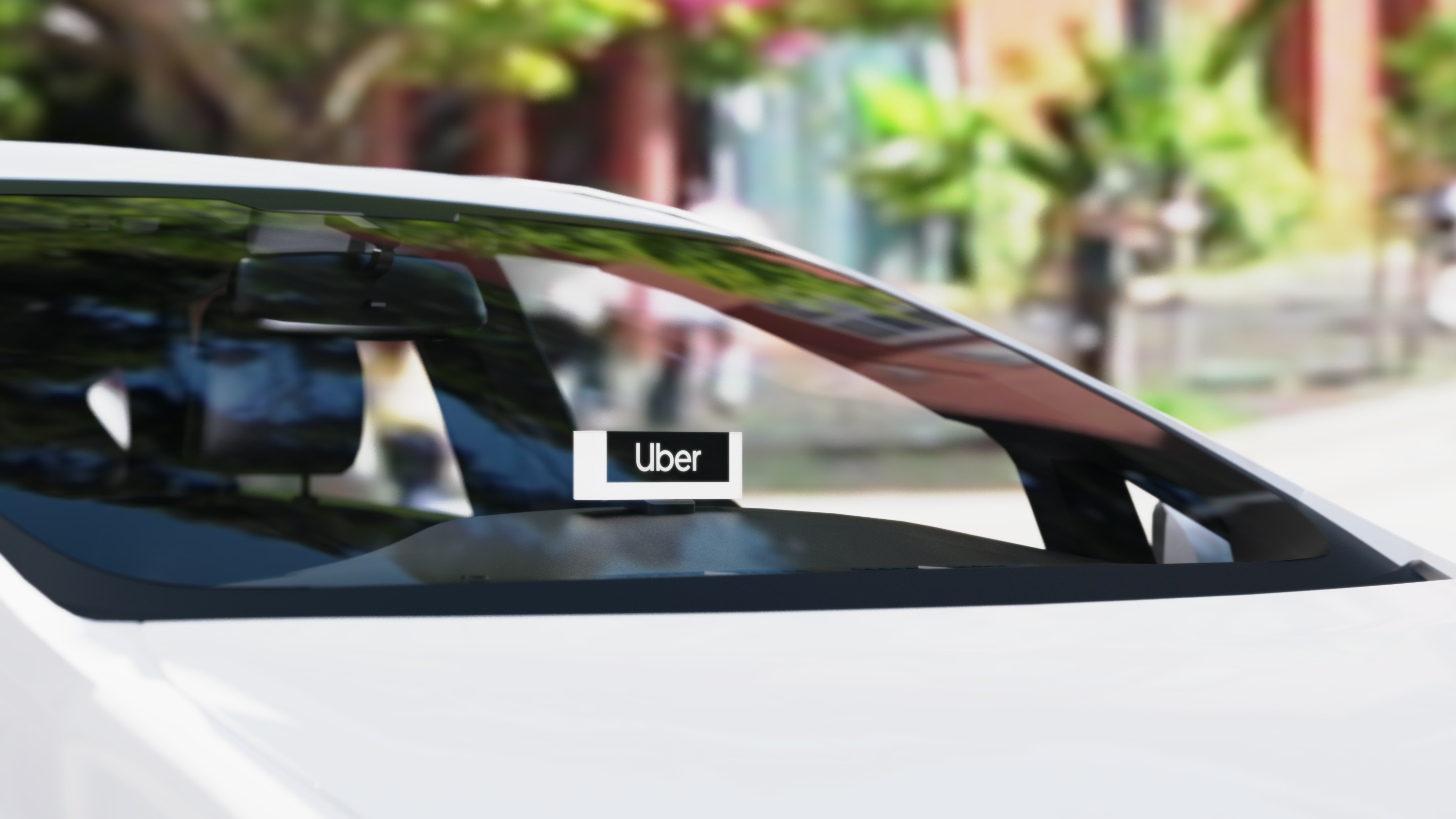 Close-up of a white car with an Uber sign displayed on the dashboard behind the windshield.