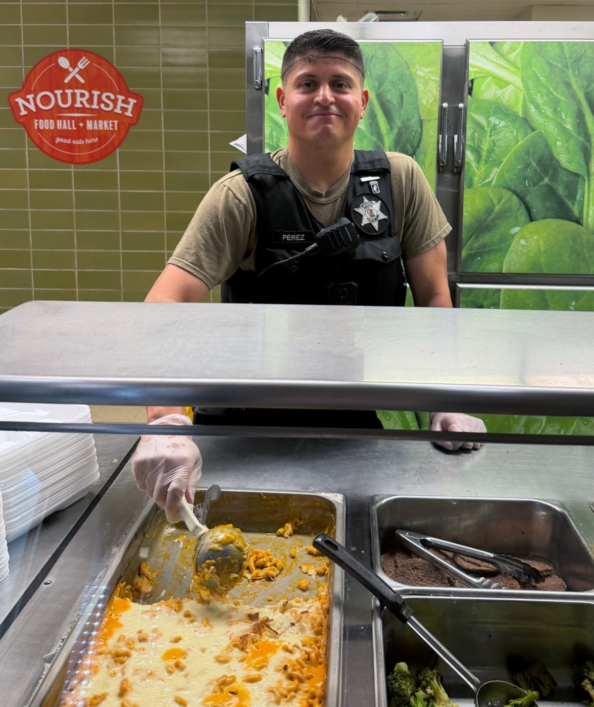Man in uniform serves lunch to students in vest.