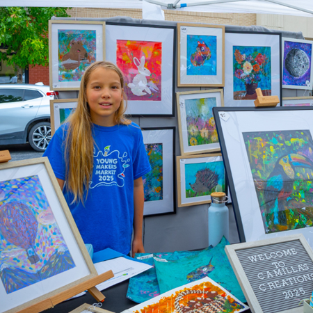 A young artist showcases colorful artwork at a community art market.
