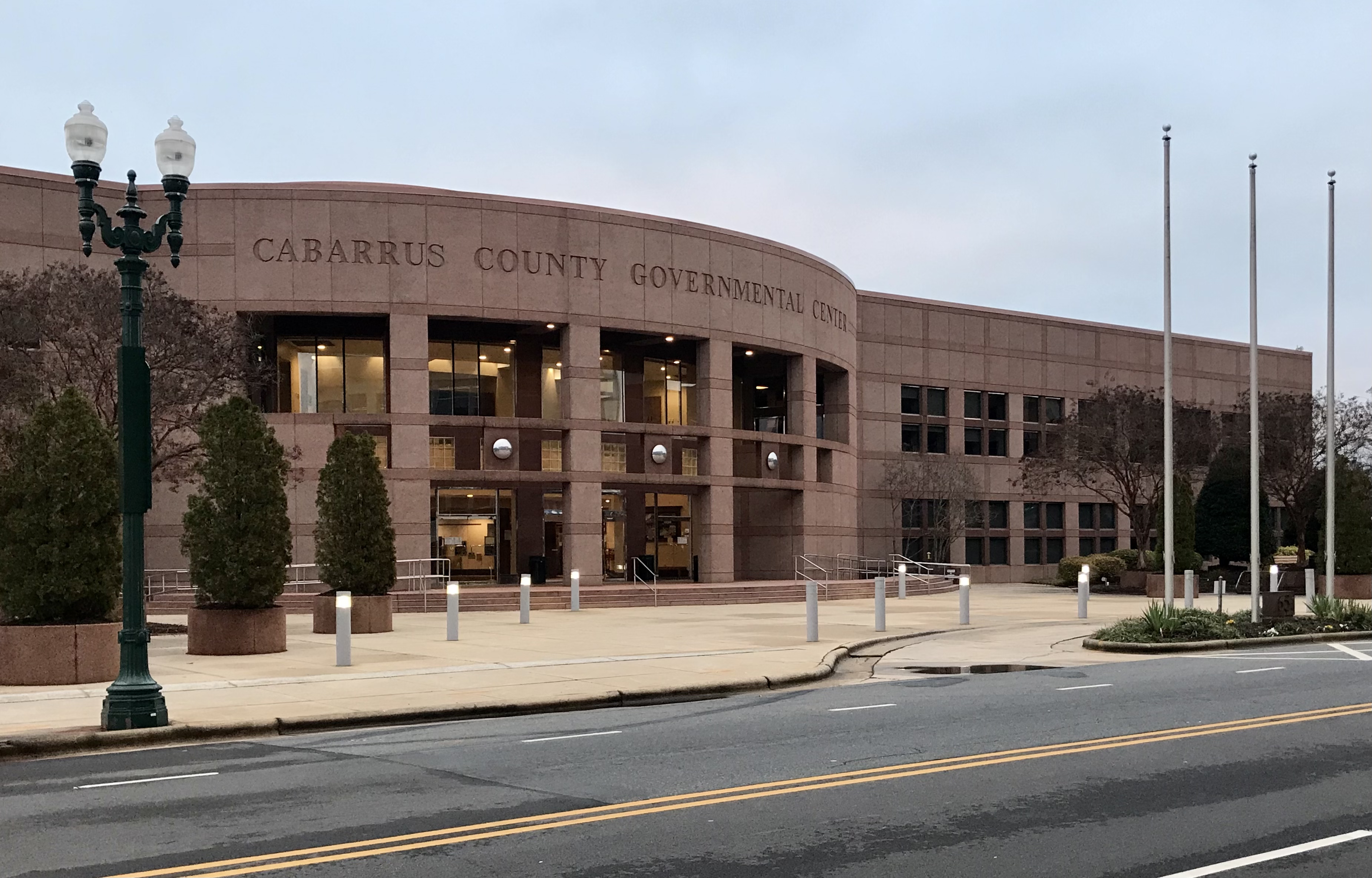 Exterior of a reddish-brown multi-story government building with flagpoles out front.