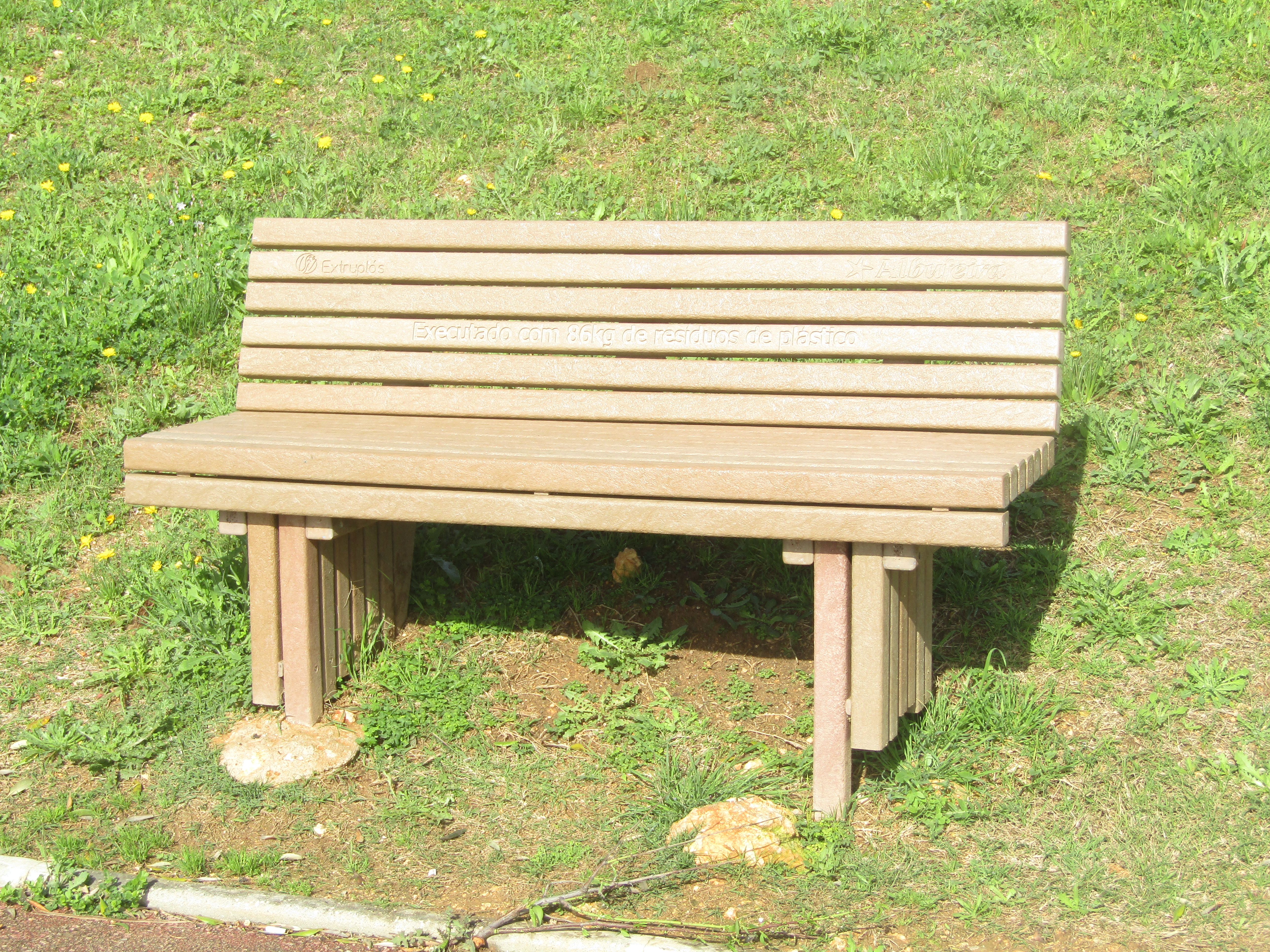 A slatted recycled plastic composite park bench sitting on a grassy area.