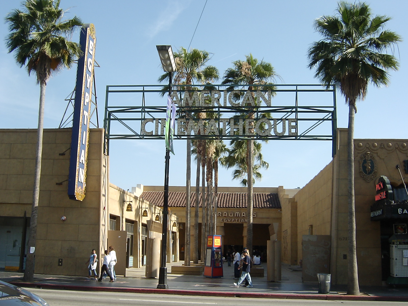Entrance to the American Cinematheque with a large overhead sign and palm trees on the sidewalk.