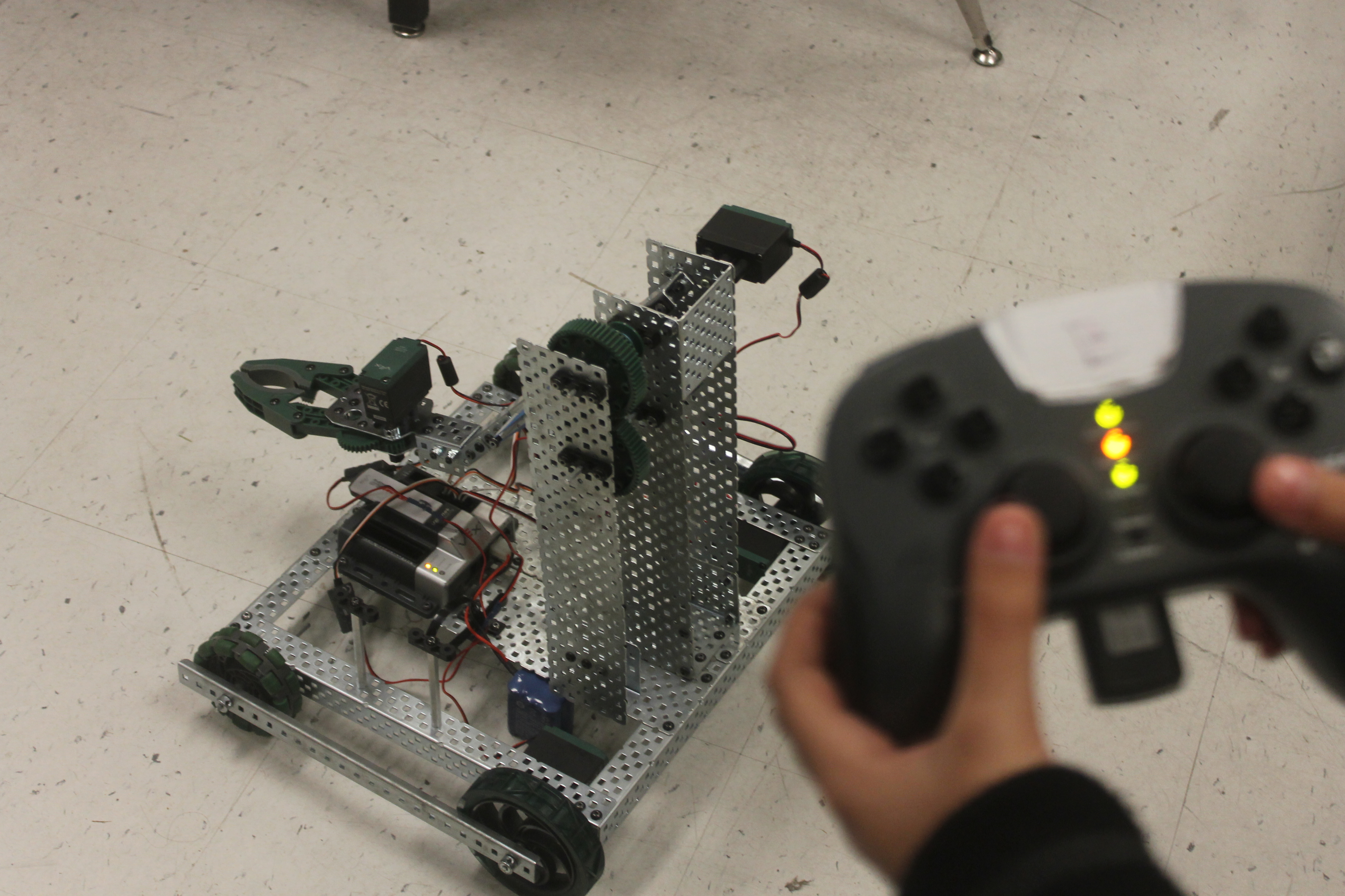 A VEX competition robot with wheels and a claw mechanism being controlled by a handheld remote.