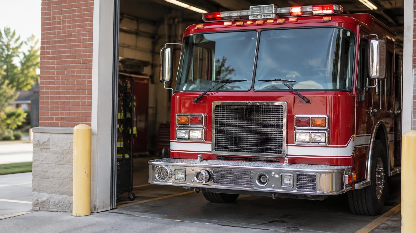 A red fire truck parked inside an open fire station bay.