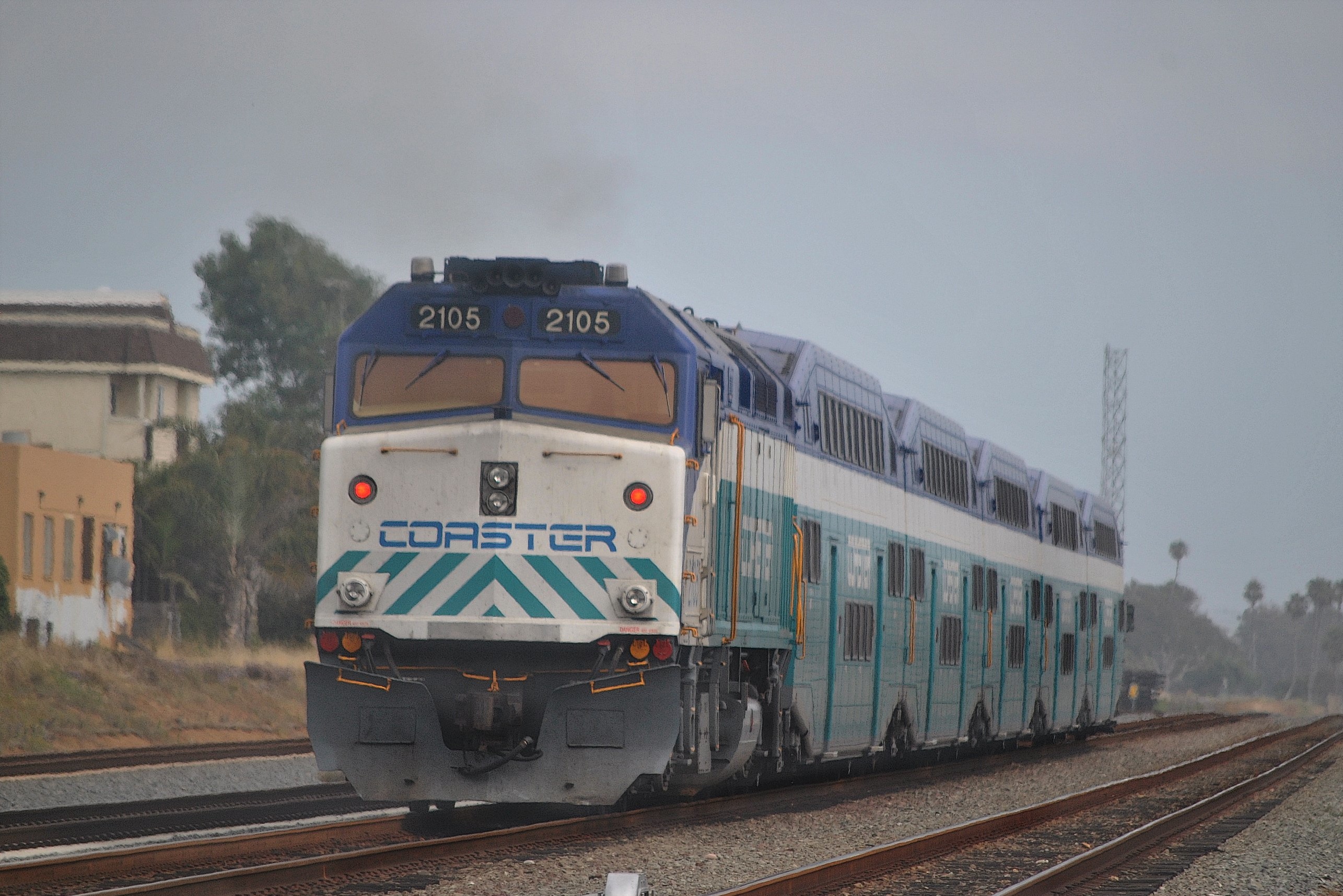 A blue and white COASTER train locomotive pulling double-deck passenger cars on a rail line.