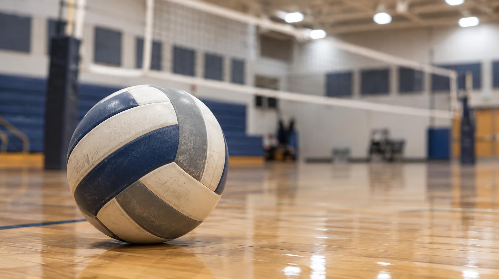 A volleyball resting on a hardwood gym floor near the net.