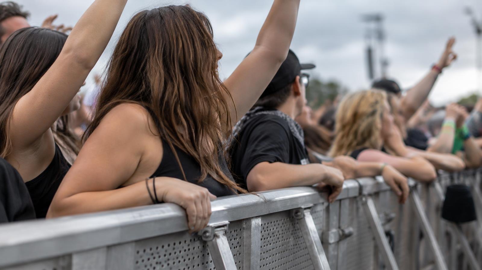 A metal crowd-control barrier fence with people pressing against it at an outdoor event.