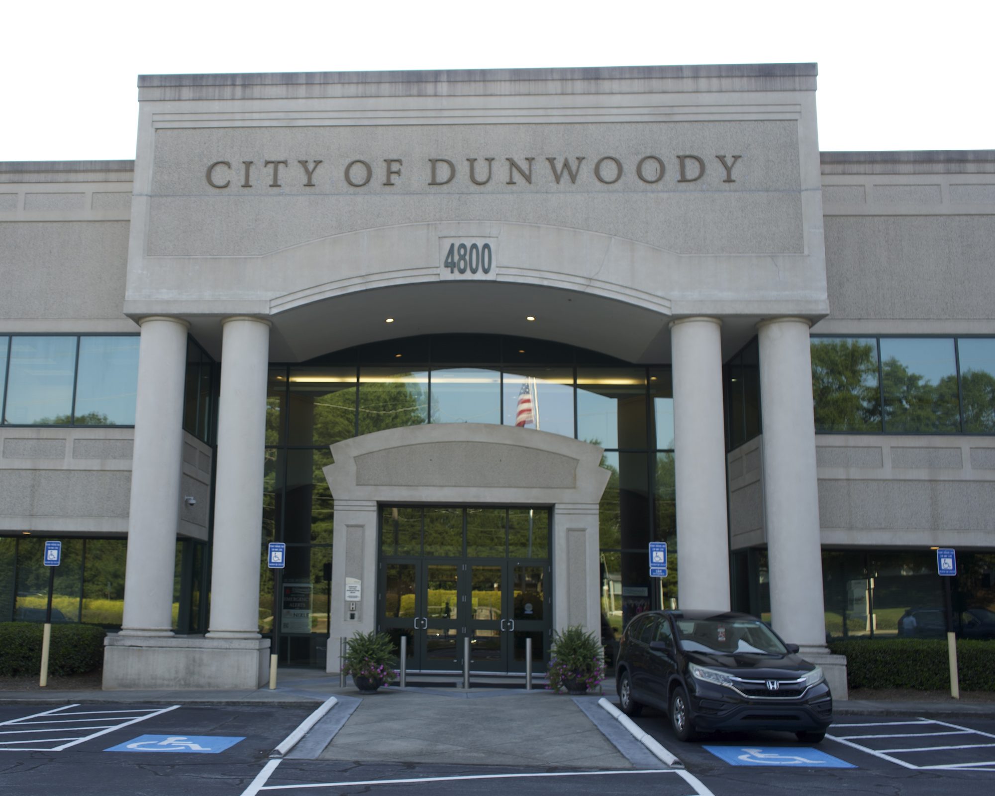 Government building entrance with stone columns and engraved city name above glass doors.