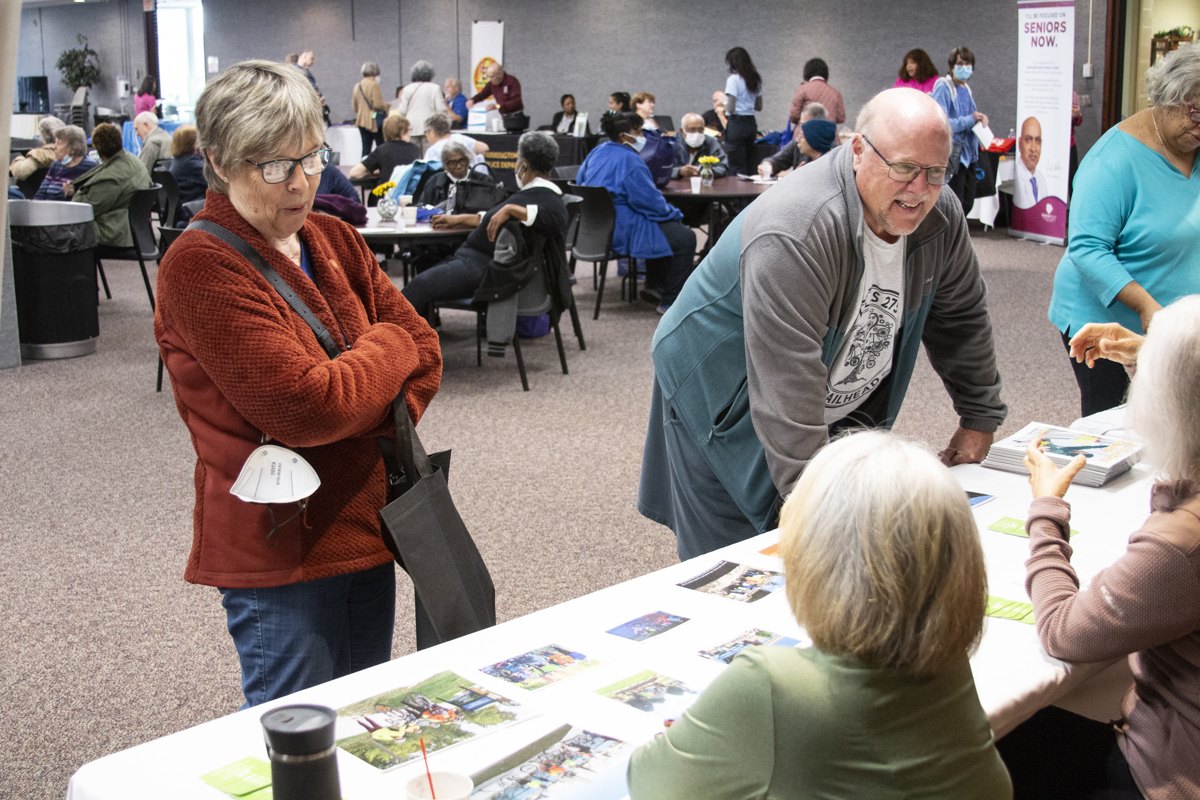 Older adults browse brochures at tables inside a large community health fair hall.