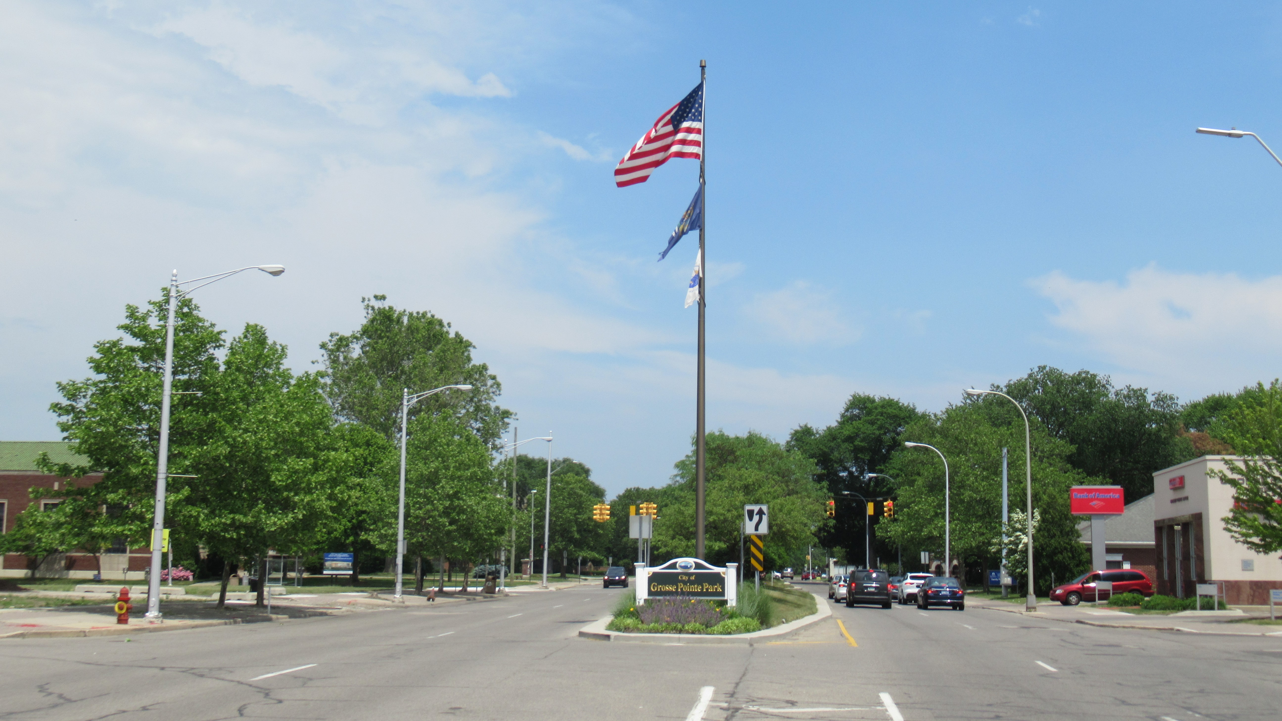 Tree-lined boulevard with a welcome sign reading Grosse Pointe Park and a flagpole.