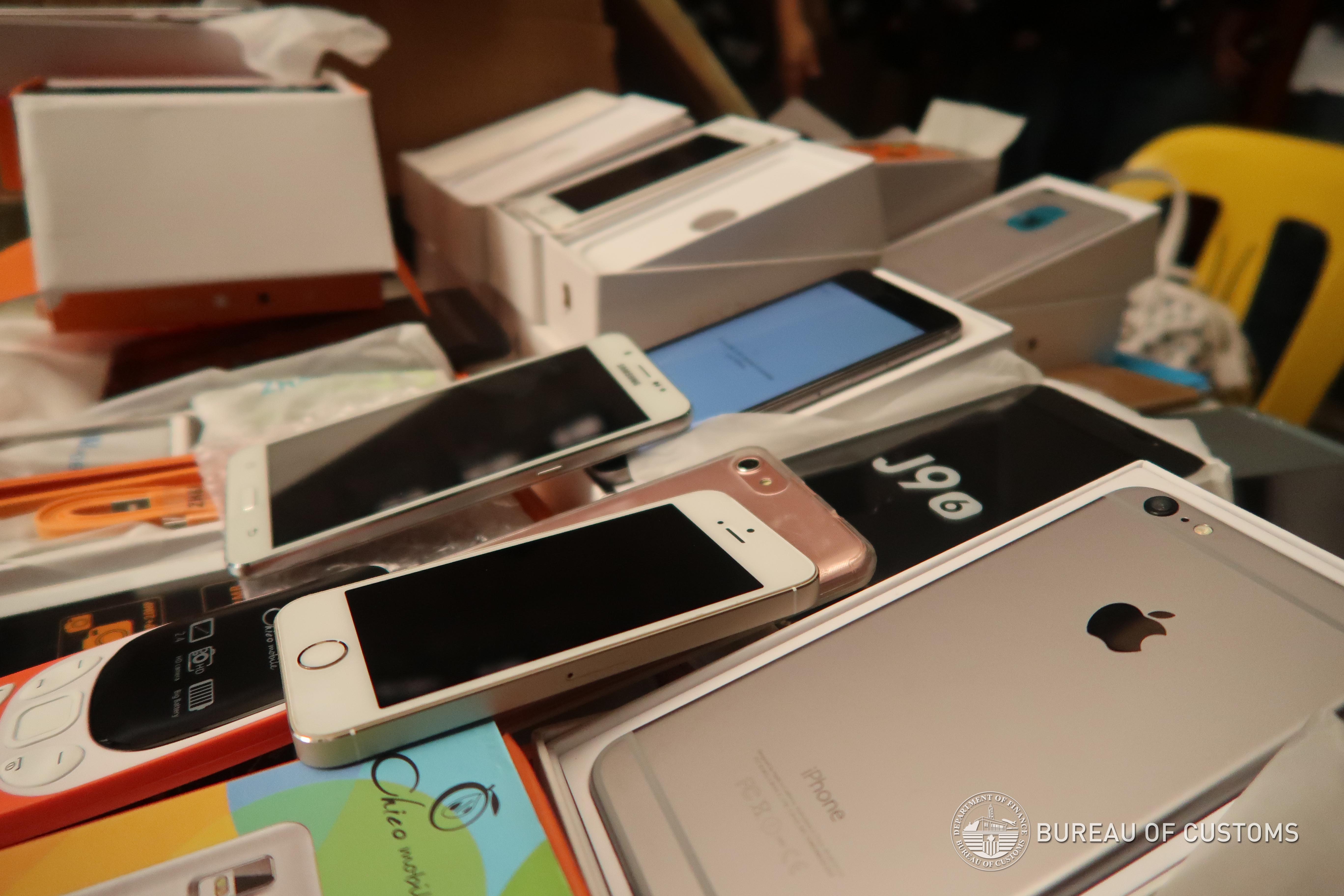 Seized counterfeit smartphones and tablets piled on a table with retail packaging boxes.
