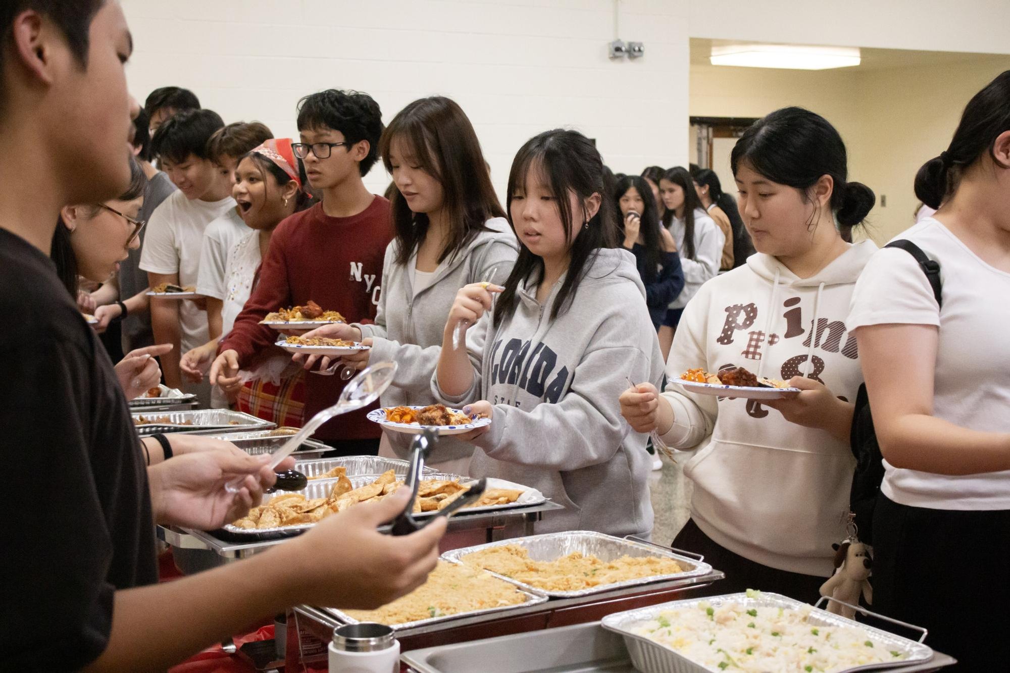 A crowd of students serving themselves food from chafing dishes at a buffet line.