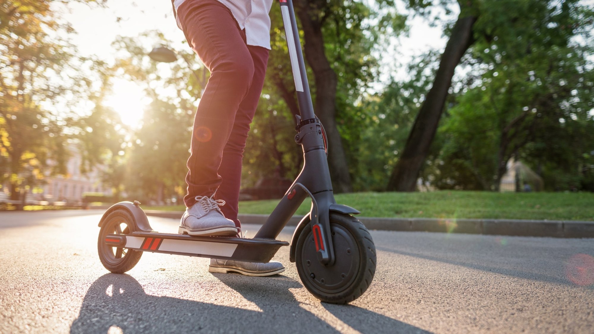 Person riding a black electric scooter on a sunny paved path.