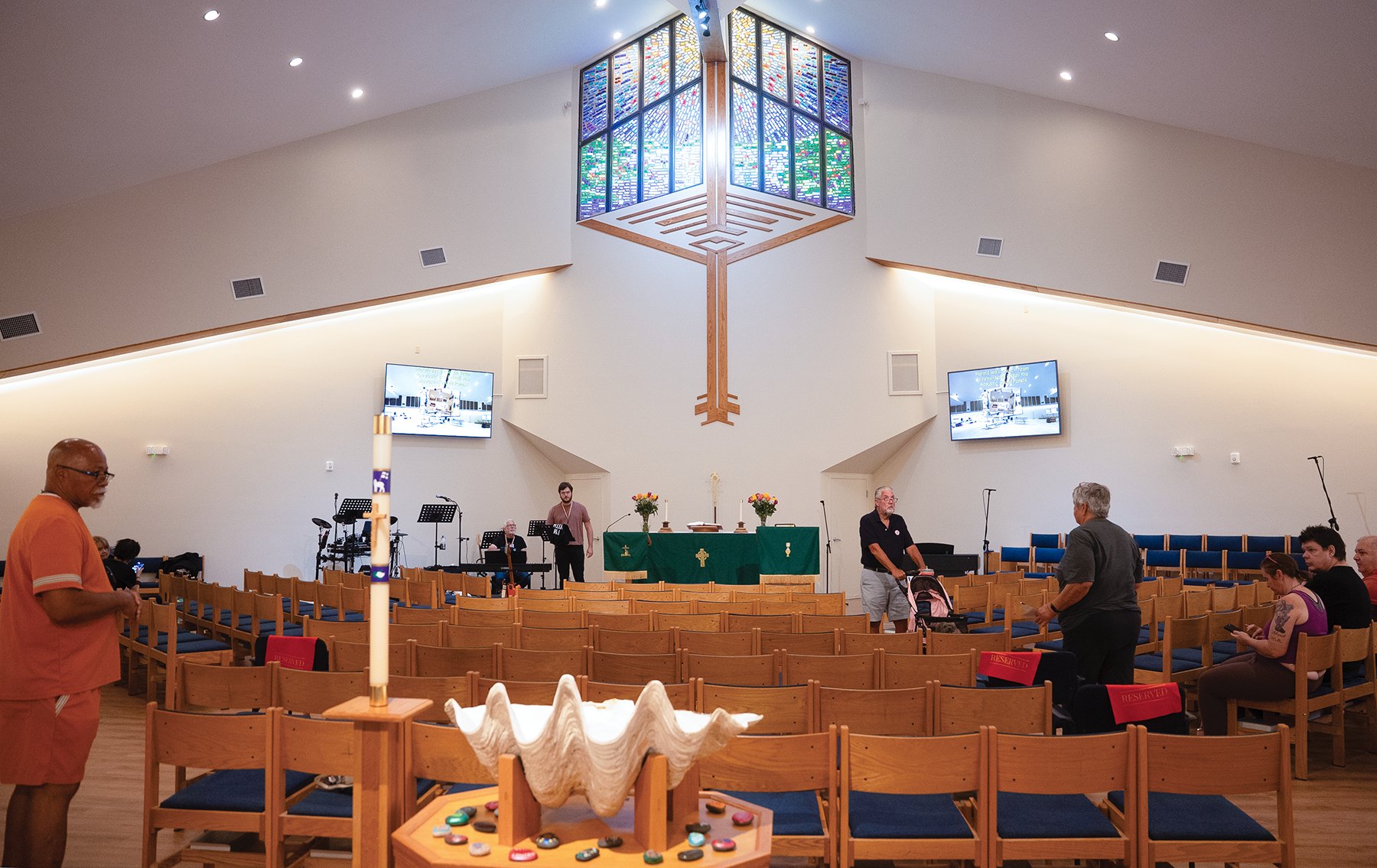 Church sanctuary interior with rows of blue-cushioned chairs facing a green-draped altar and suspended stained-glass lantern.