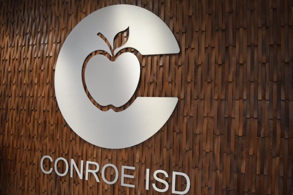 Silver circular school district logo mounted on a wood-panel wall with text below.
