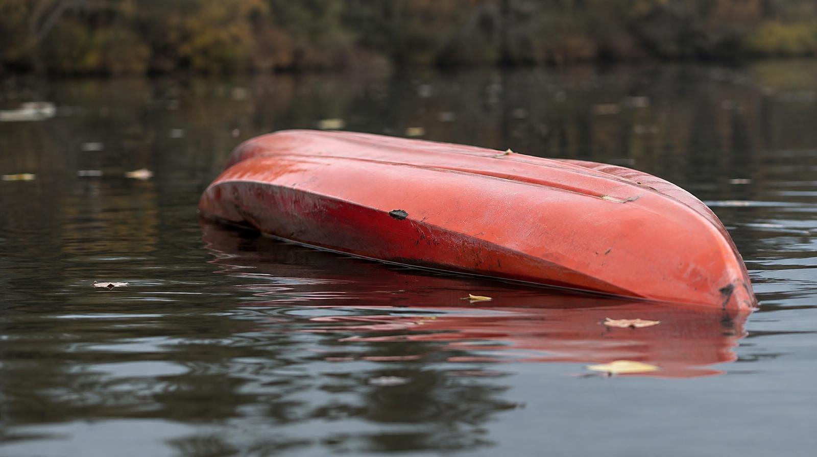 An overturned kayak floating on a dark, calm pond with no one nearby.