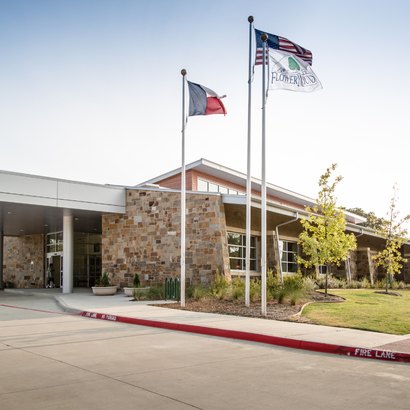 Exterior of a stone-clad public building with three flagpoles out front.