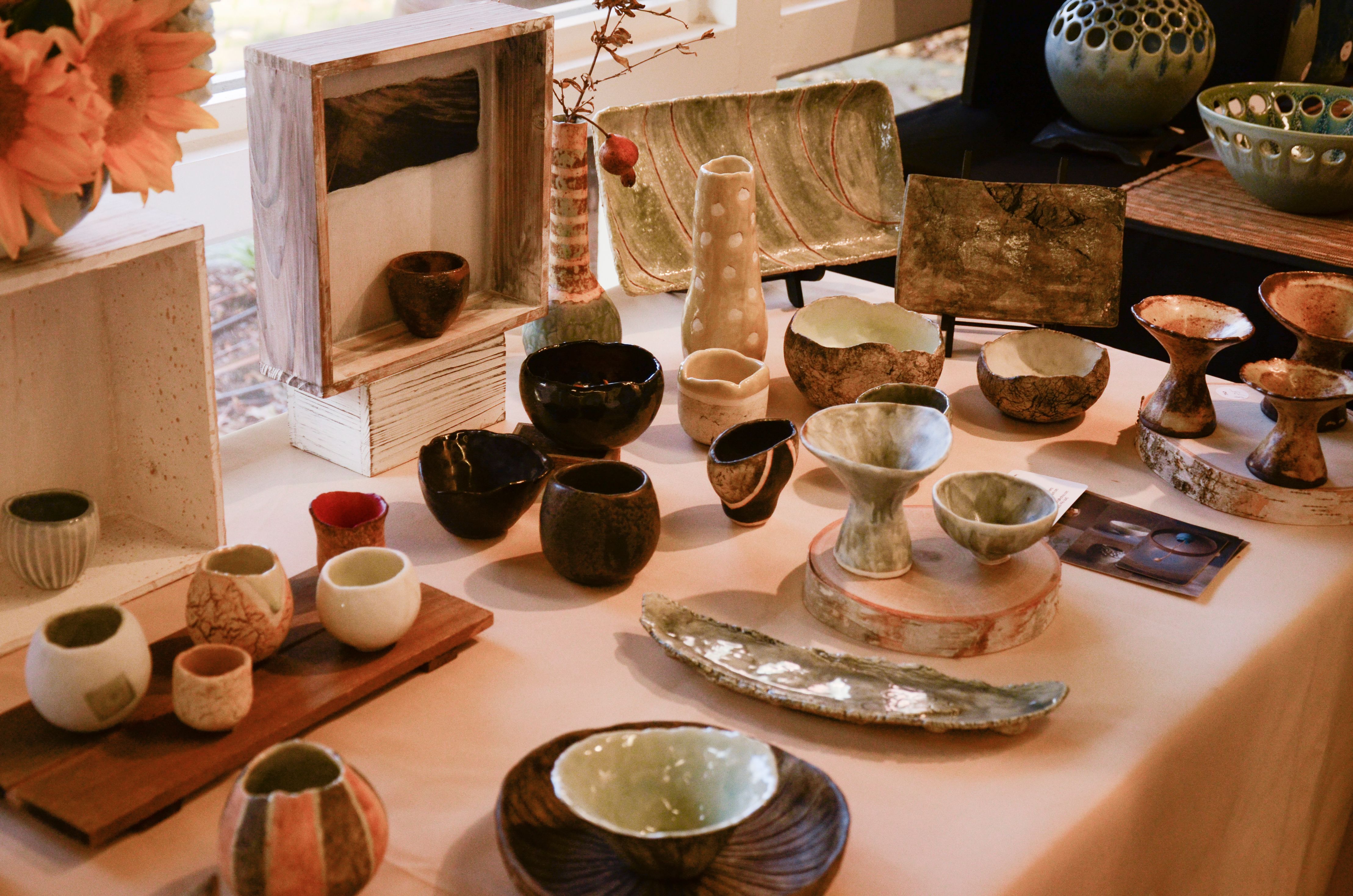 Handmade ceramic bowls, vases, and plates arranged on a white-covered display table.