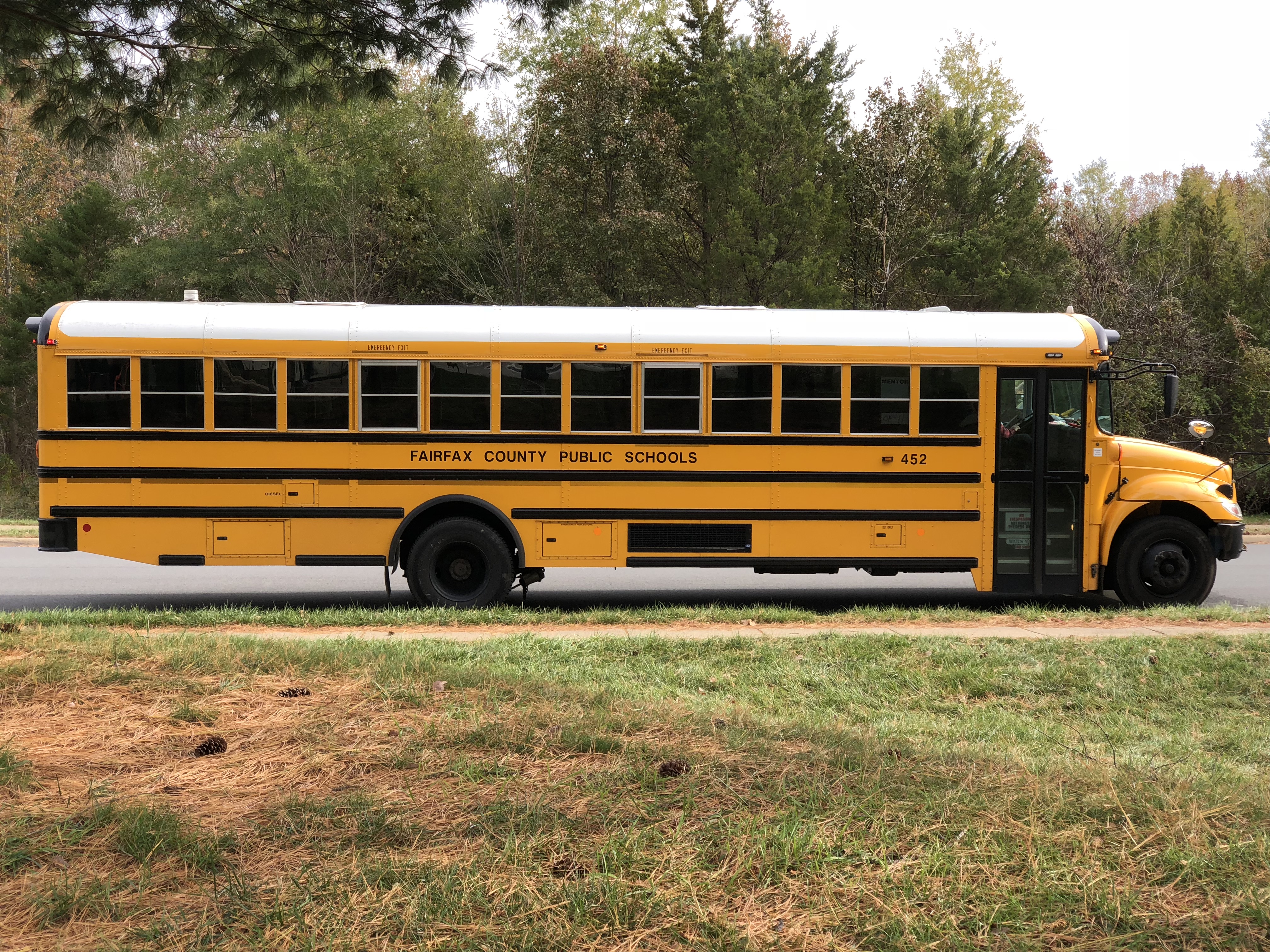 A yellow Fairfax County Public Schools school bus traveling along a tree-lined road.