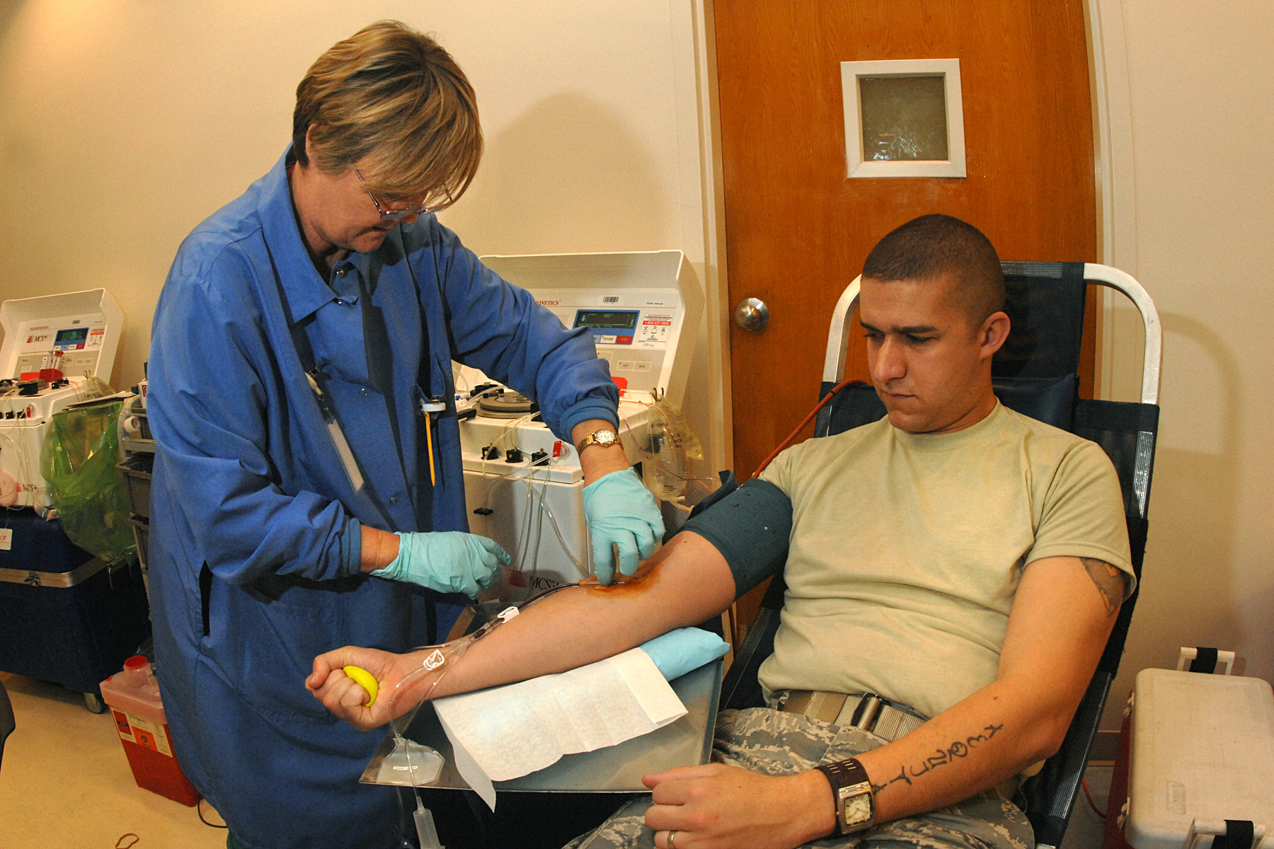 A phlebotomist in blue gloves attends to a donor's arm during a blood drive.