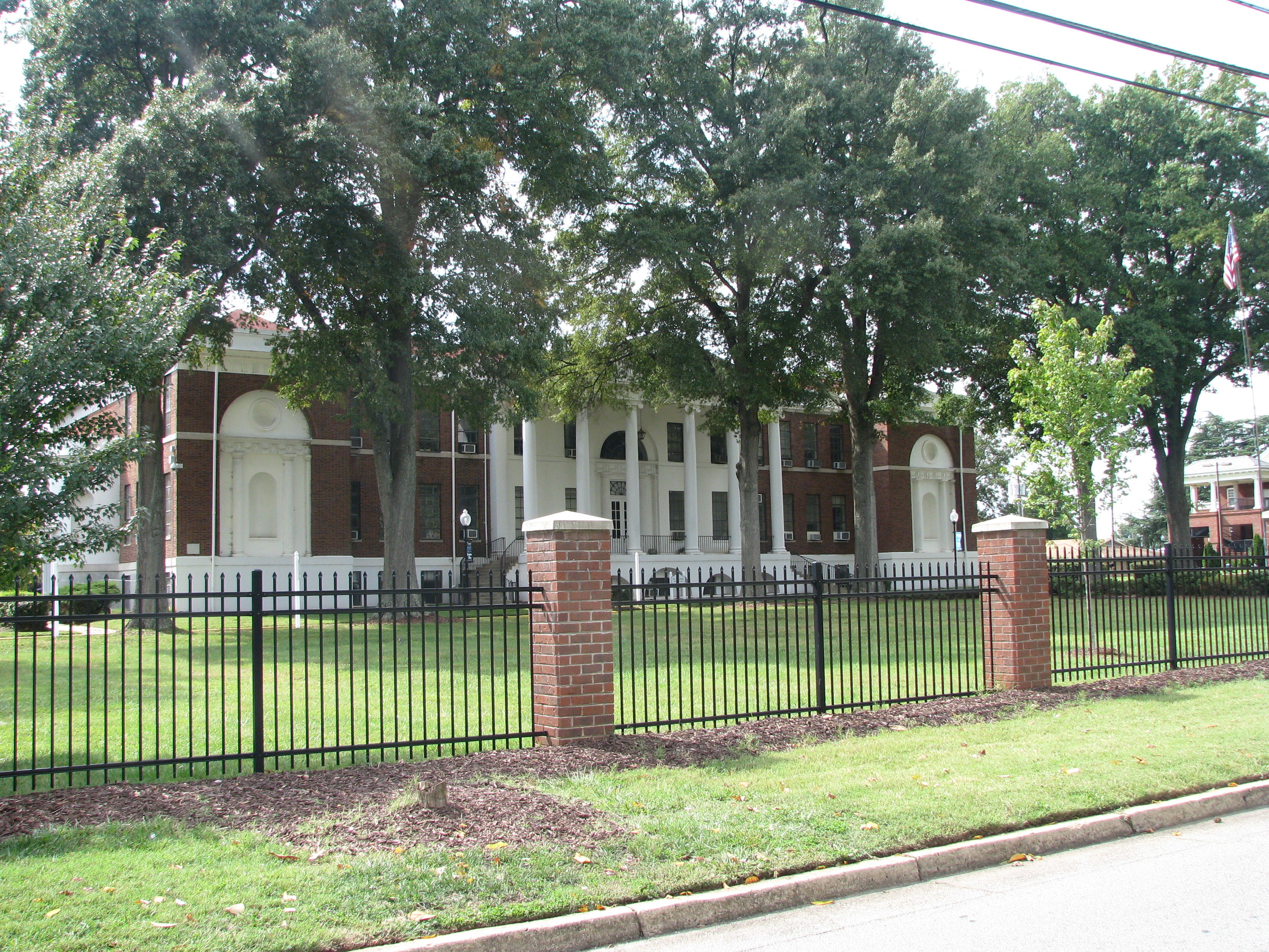 Brick building with white neoclassical columns behind an iron fence on a college campus.