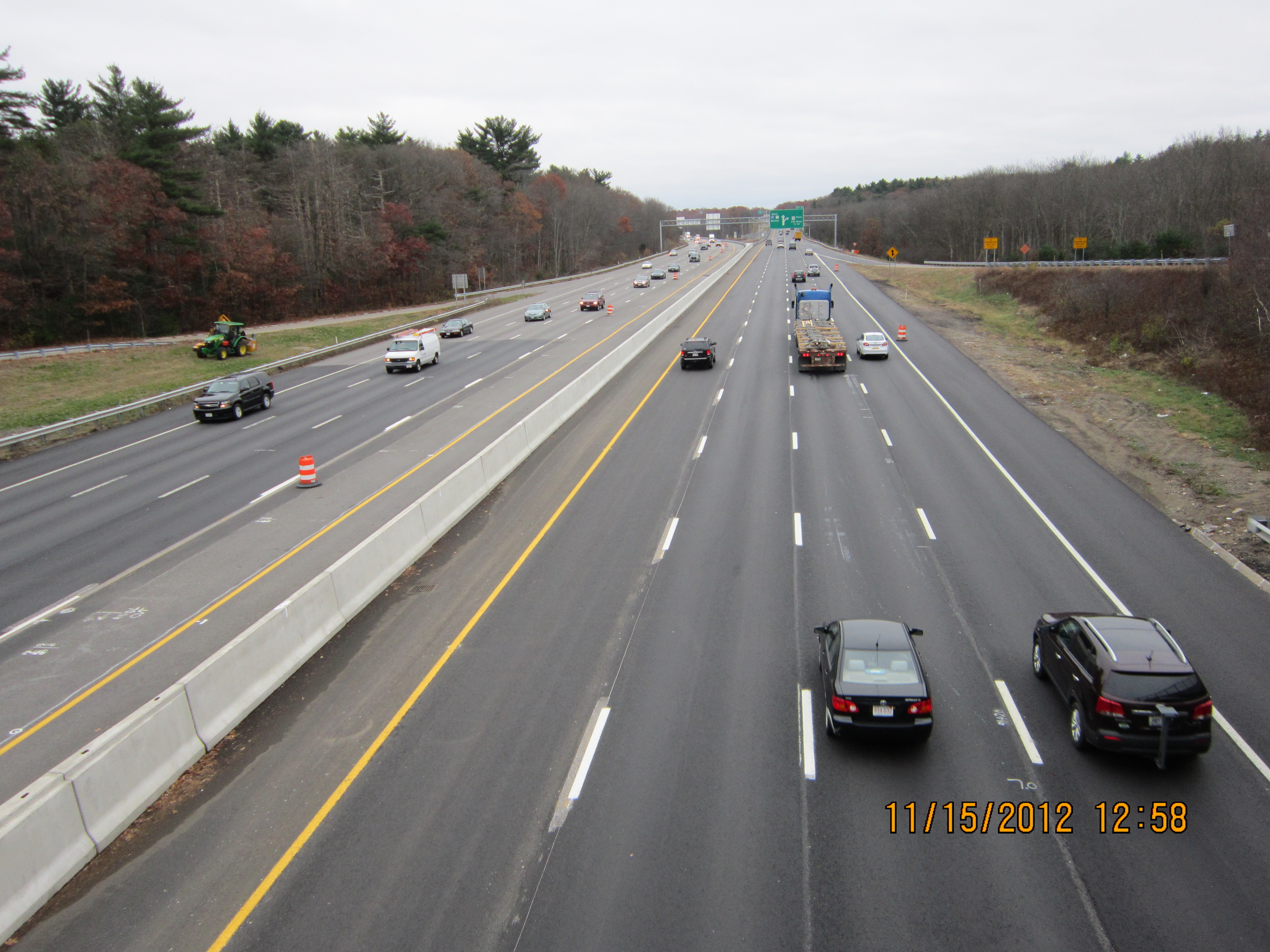Multi-lane highway with vehicles traveling in both directions, viewed from an overpass with fall foliage.