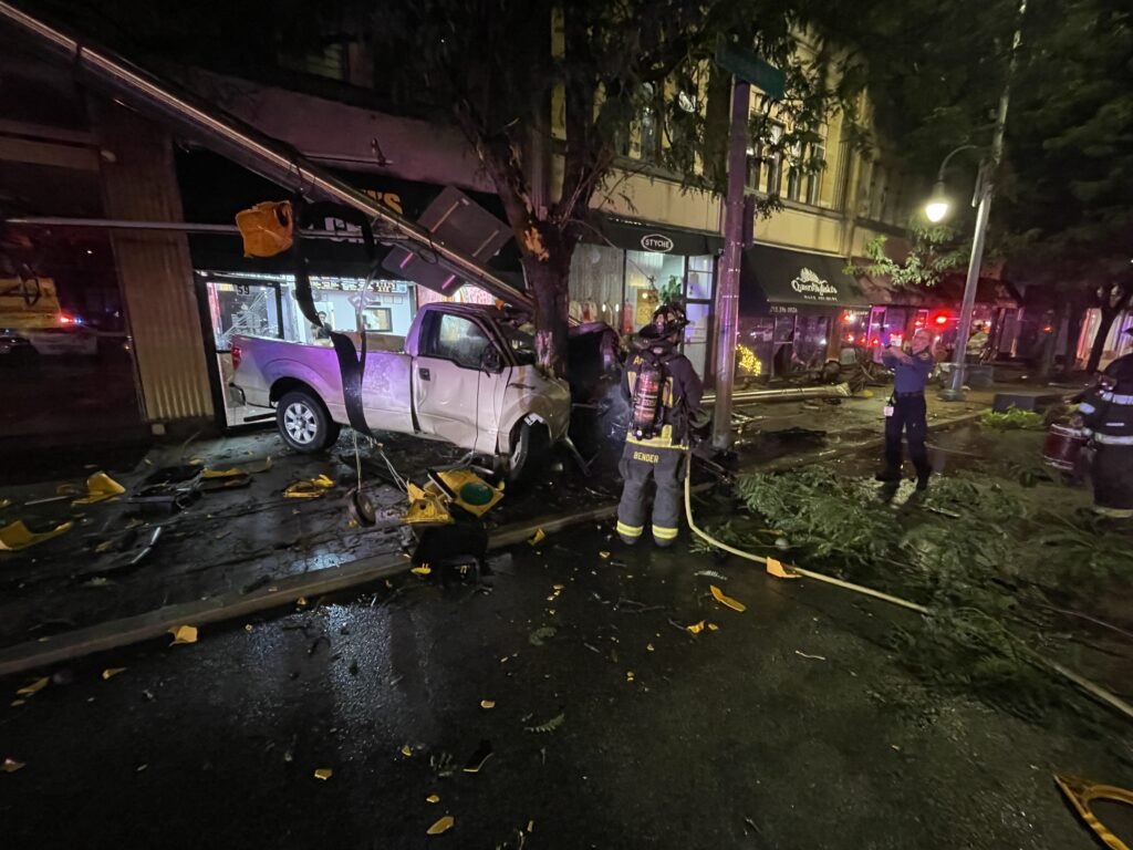 White pickup truck lodged in a storefront at night with firefighters working the scene.