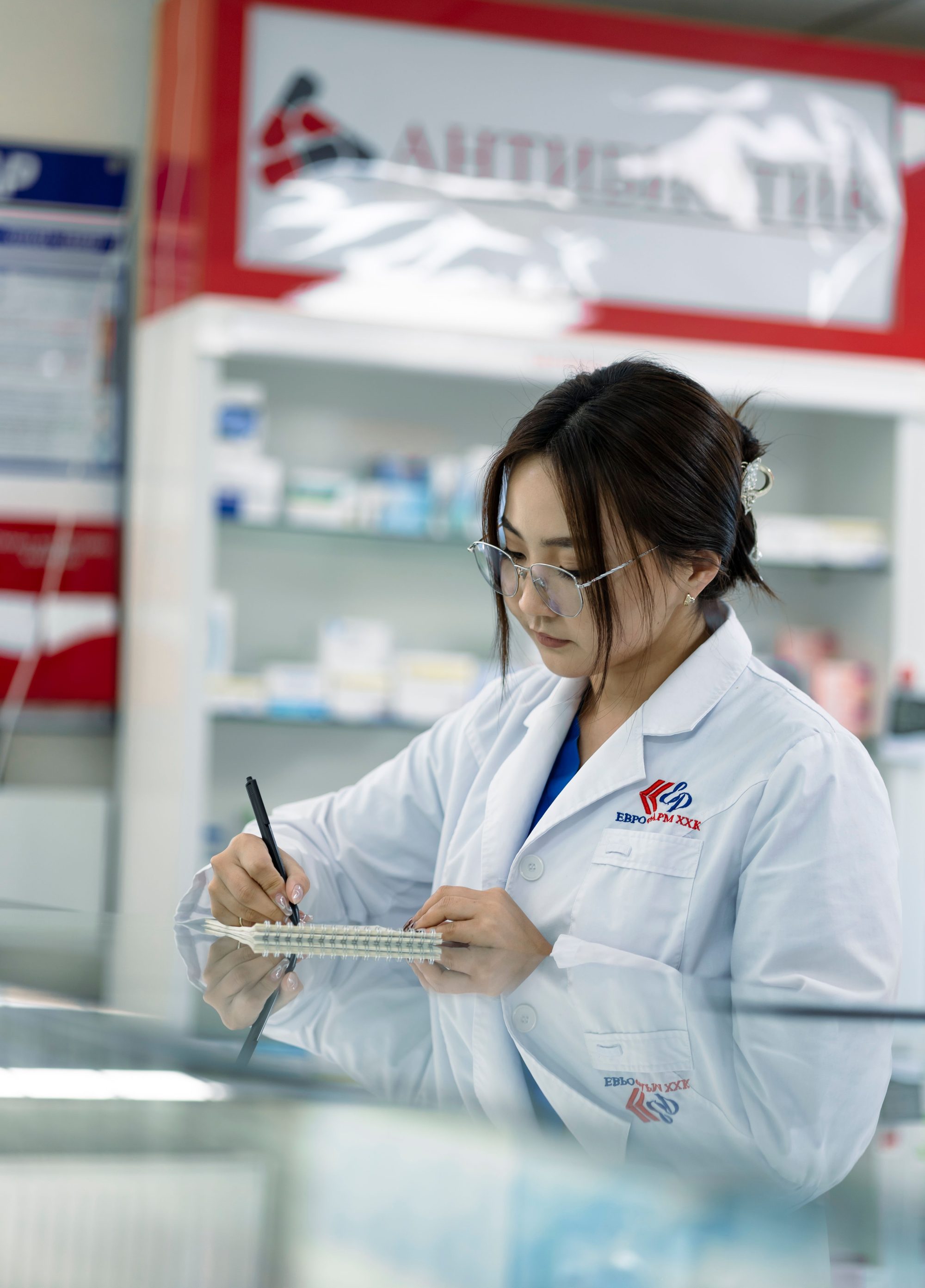 Female pharmacist taking notes in a pharmacy environment.