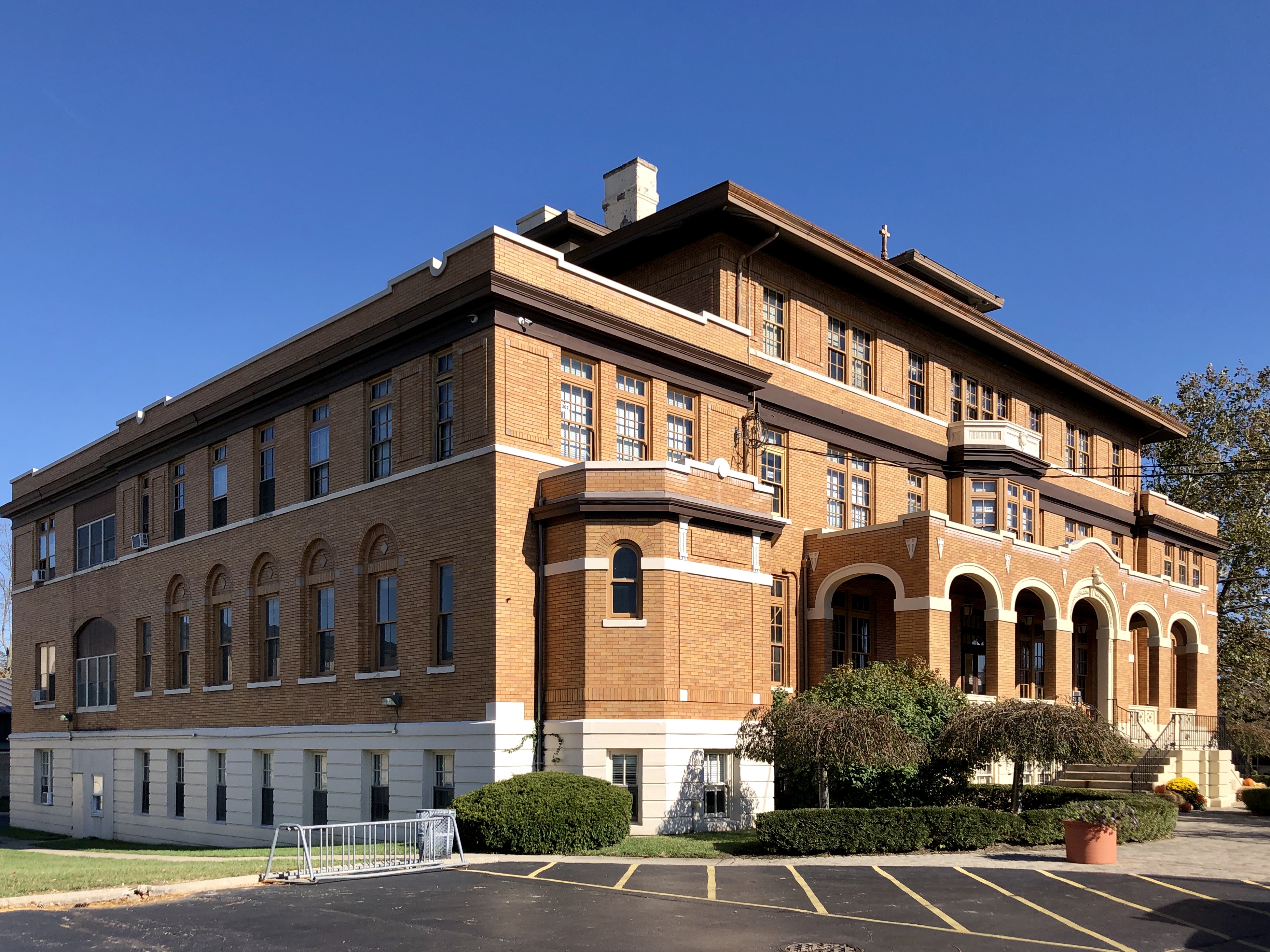 Three-story red brick school building with arched entrance and autumn trees