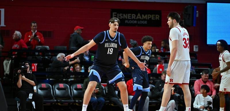 A very tall basketball player in a Villanova jersey stands on the court near an opposing player.